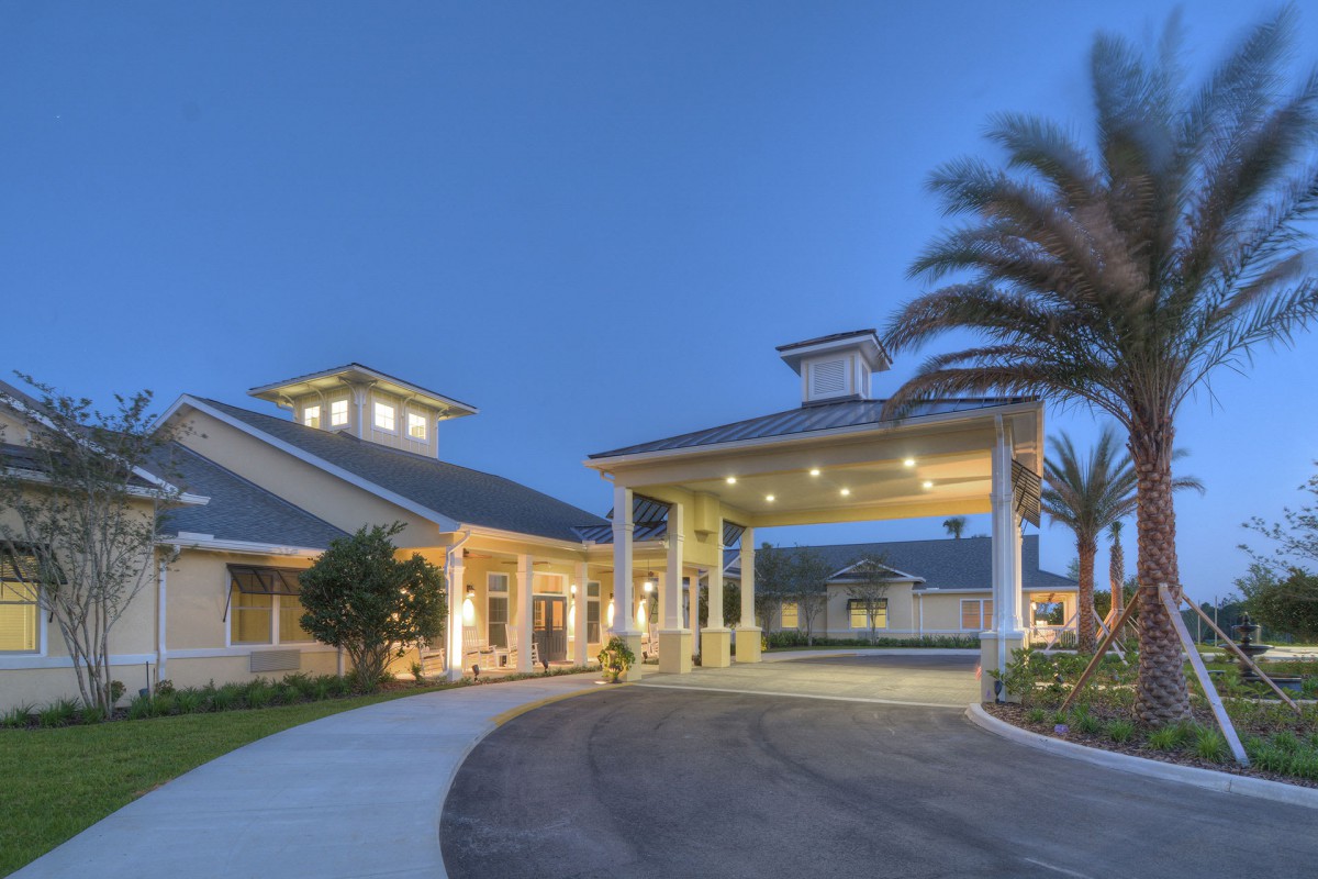 A well-lit building entrance with palm trees and a circular driveway in the evening.