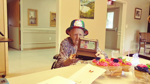 An elderly individual wearing a colorful hat, joyfully holding a small decorative item at a table.