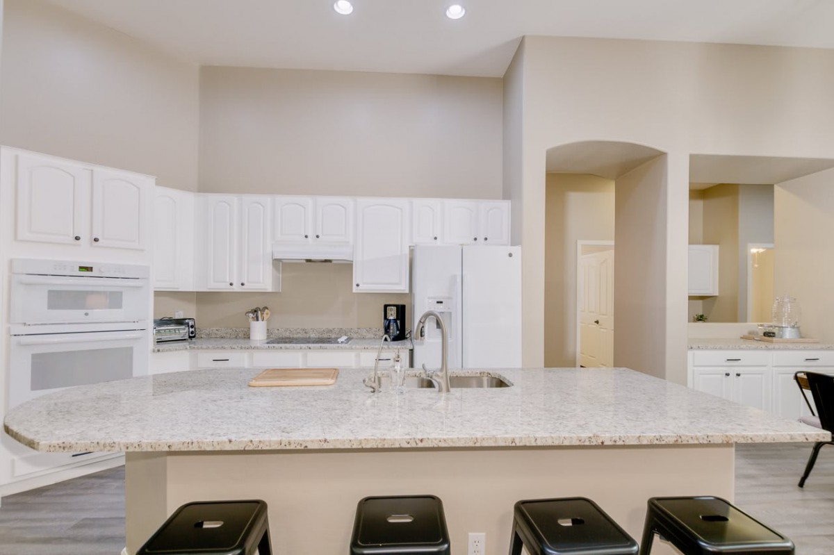 A modern kitchen with white cabinets and a spacious countertop, featuring several black stools for seating.