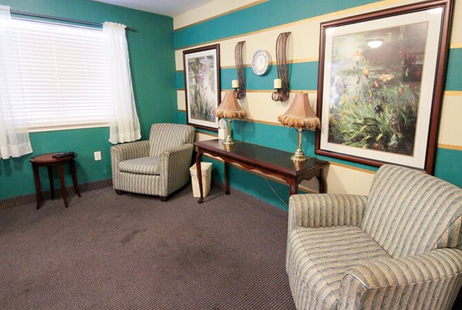 A cozy living room with striped walls featuring armchairs, a wooden table adorned with lamps, and framed artwork.