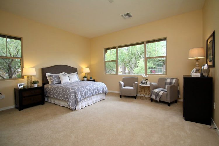 A spacious bedroom with a large bed, two chairs by the window, and soft lighting.