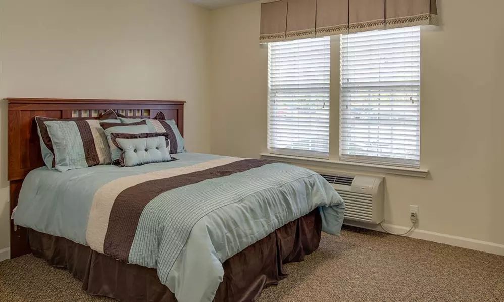 A cozy bedroom with a neatly made bed and large window blinds.