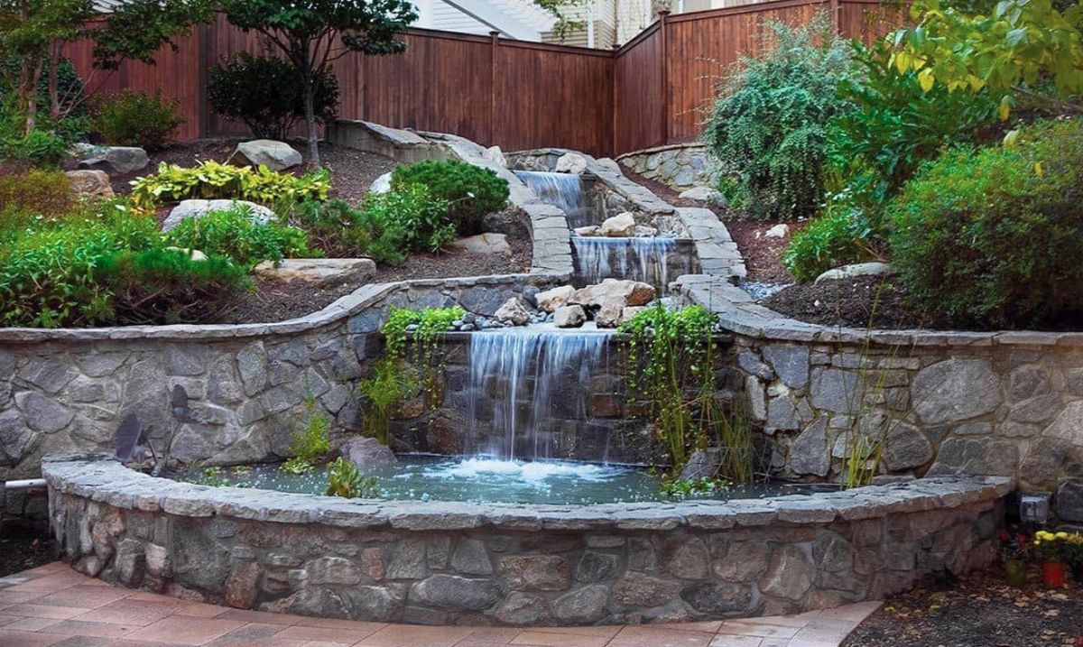 A beautiful garden waterfall with stone walls and lush greenery.