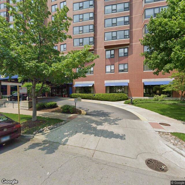 An apartment building with a driveway and parked cars surrounded by greenery.
