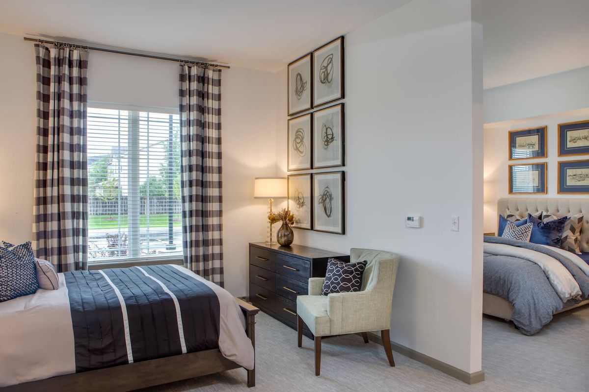 A modern bedroom with stylish decor, featuring a bed, dresser, armchair, and artwork.