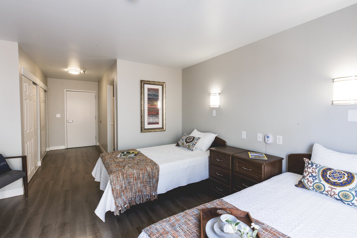 A modern hotel room featuring twin beds with elegant decor and wooden flooring.