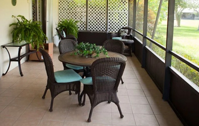 A cozy outdoor patio with a wicker table and chairs, surrounded by plants.