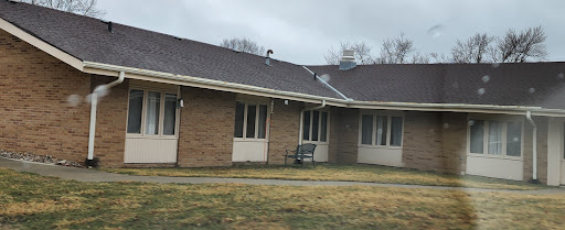 A view of a brick residential building with a bench in front and cloudy skies overhead.