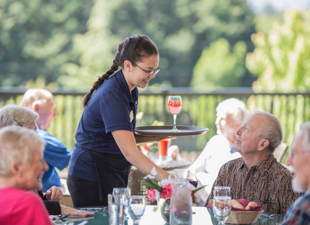 A waitress serves drinks to customers at an outdoor restaurant.