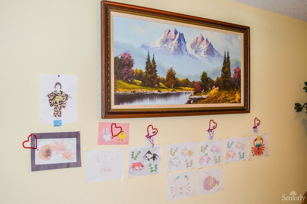 A wall decorated with a mountain landscape painting and children's drawings.