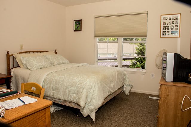 A cozy, well-lit bedroom with a bed, nightstand, and window featuring blinds.