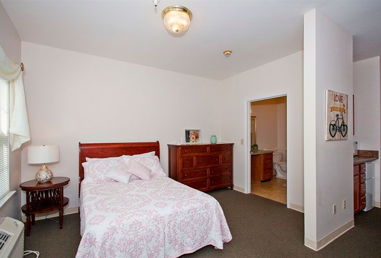 A cozy bedroom with a bed, wooden dresser, and an open door leading to a bathroom.
