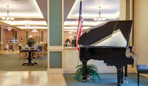 A grand piano in a lobby with an American flag and elegant decor.
