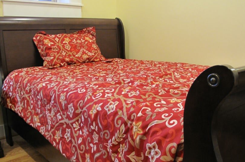 A cozy bedroom with a red patterned bedspread and matching pillow on a dark wooden bed frame.