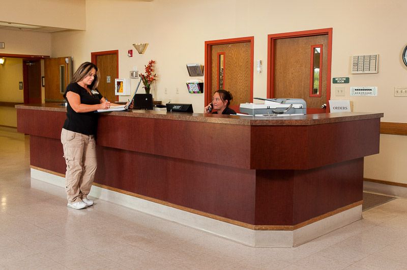 A receptionist assisting a visitor at the front desk of an office.