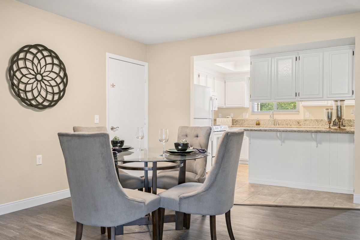 A modern dining area with a glass table and upholstered chairs, seamlessly connected to a bright kitchen.