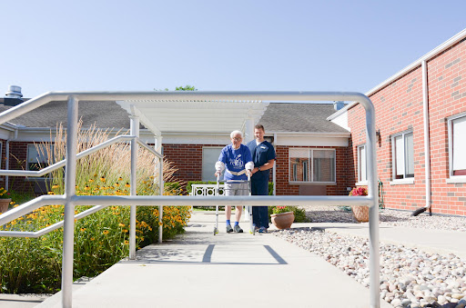 A caregiver assists a senior individual as they walk outside, showcasing the importance of support in rehabilitation.