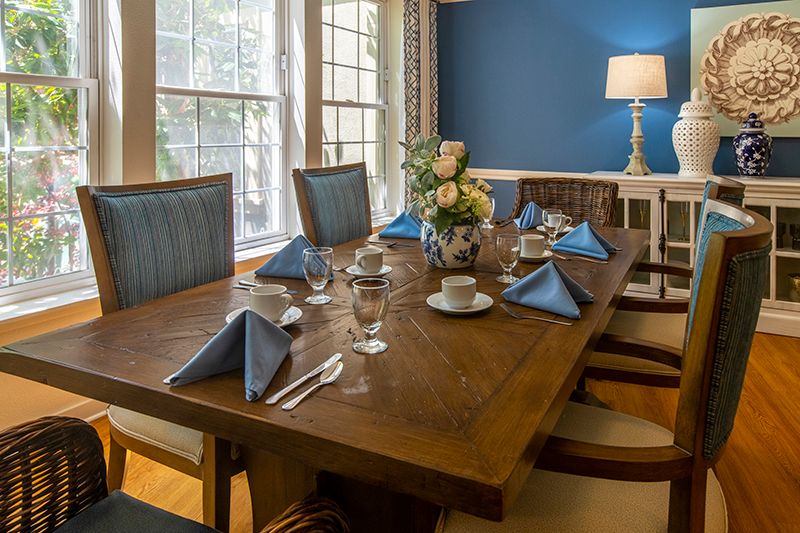 A dining room with a beautifully set wooden table, featuring blue napkins and floral centerpiece.