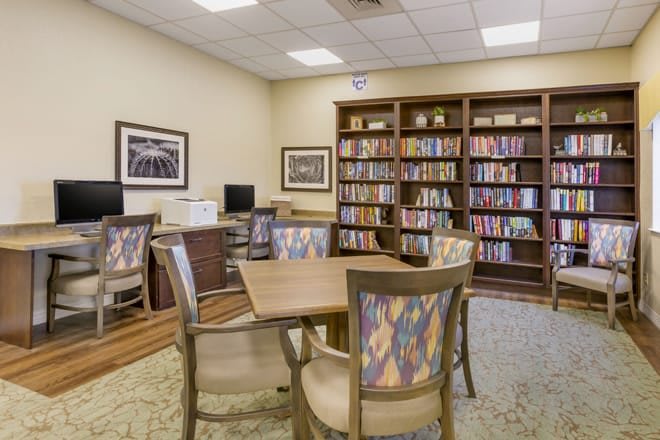 A cozy library room featuring bookshelves, computers, and a table with chairs.