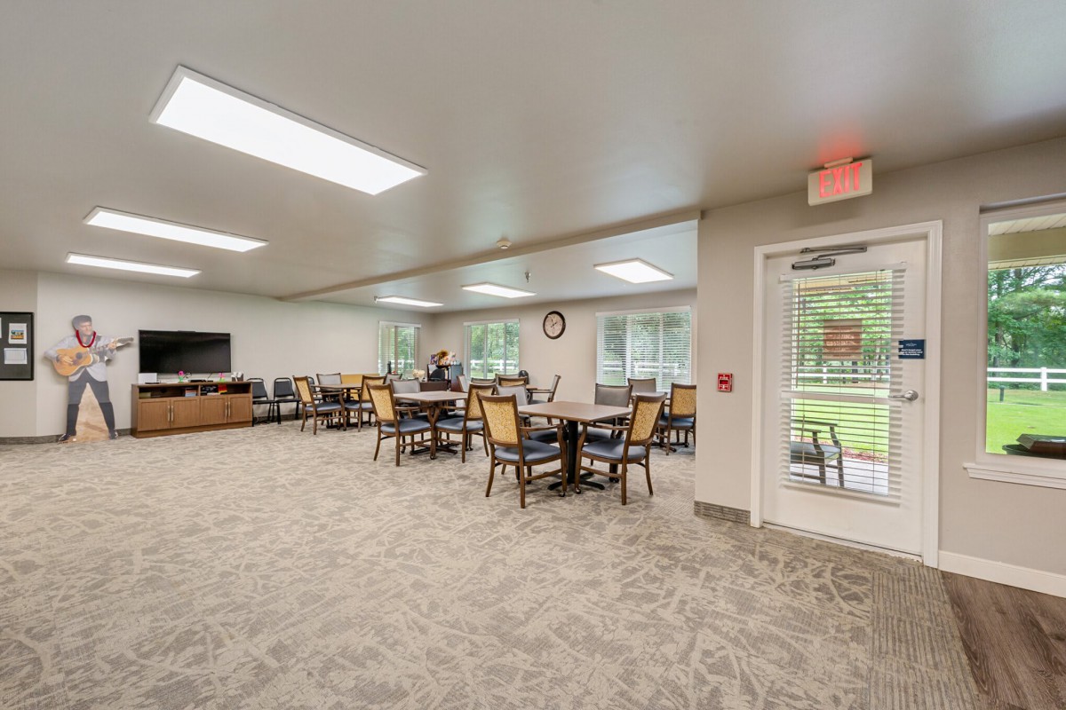 A spacious dining area with tables and chairs, featuring large windows that allow natural light to fill the room.