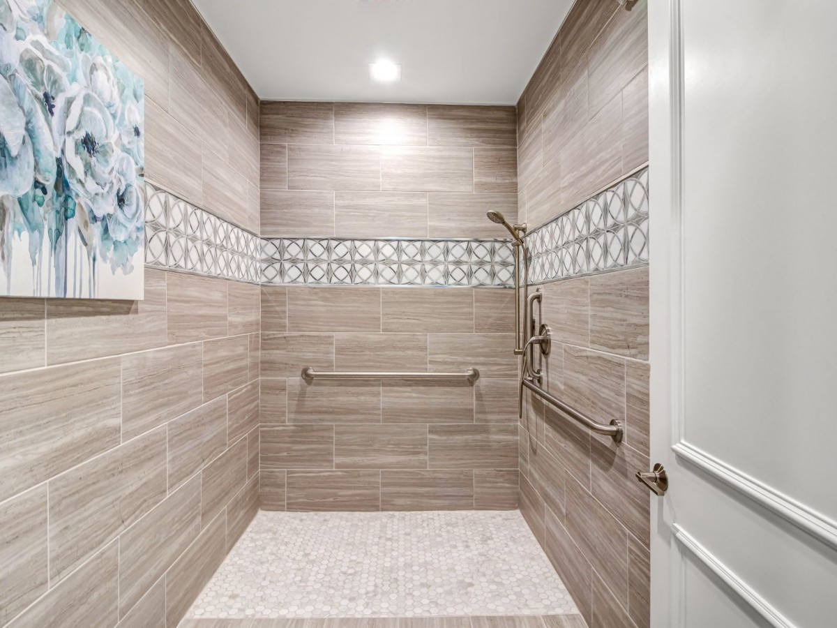 A modern walk-in shower with tiled walls, decorative border, and safety features.