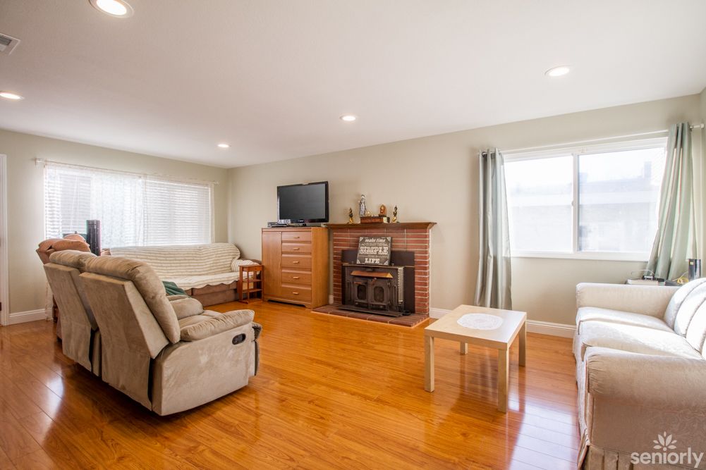 A cozy living room with hardwood floors, featuring a fireplace, sofa, recliner, and a television.