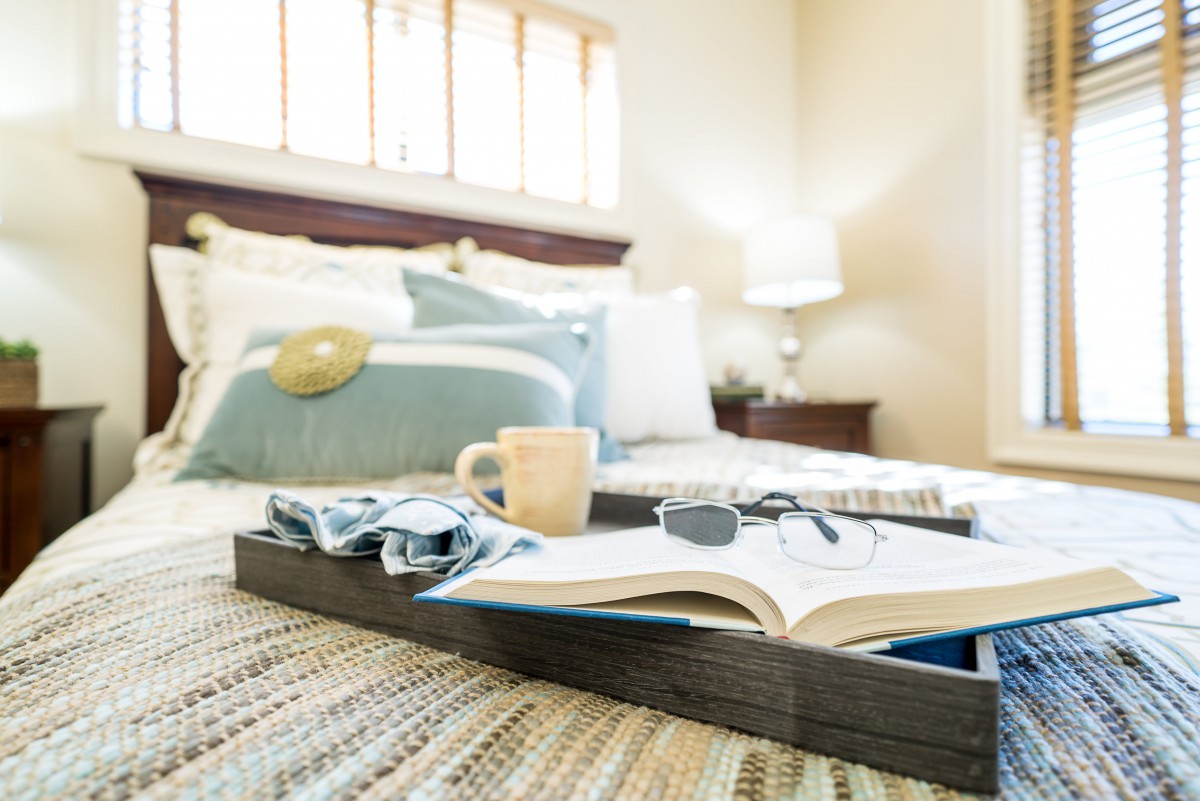 A cozy bedroom setting with a tray holding a book, coffee cup, and glasses on the bed.