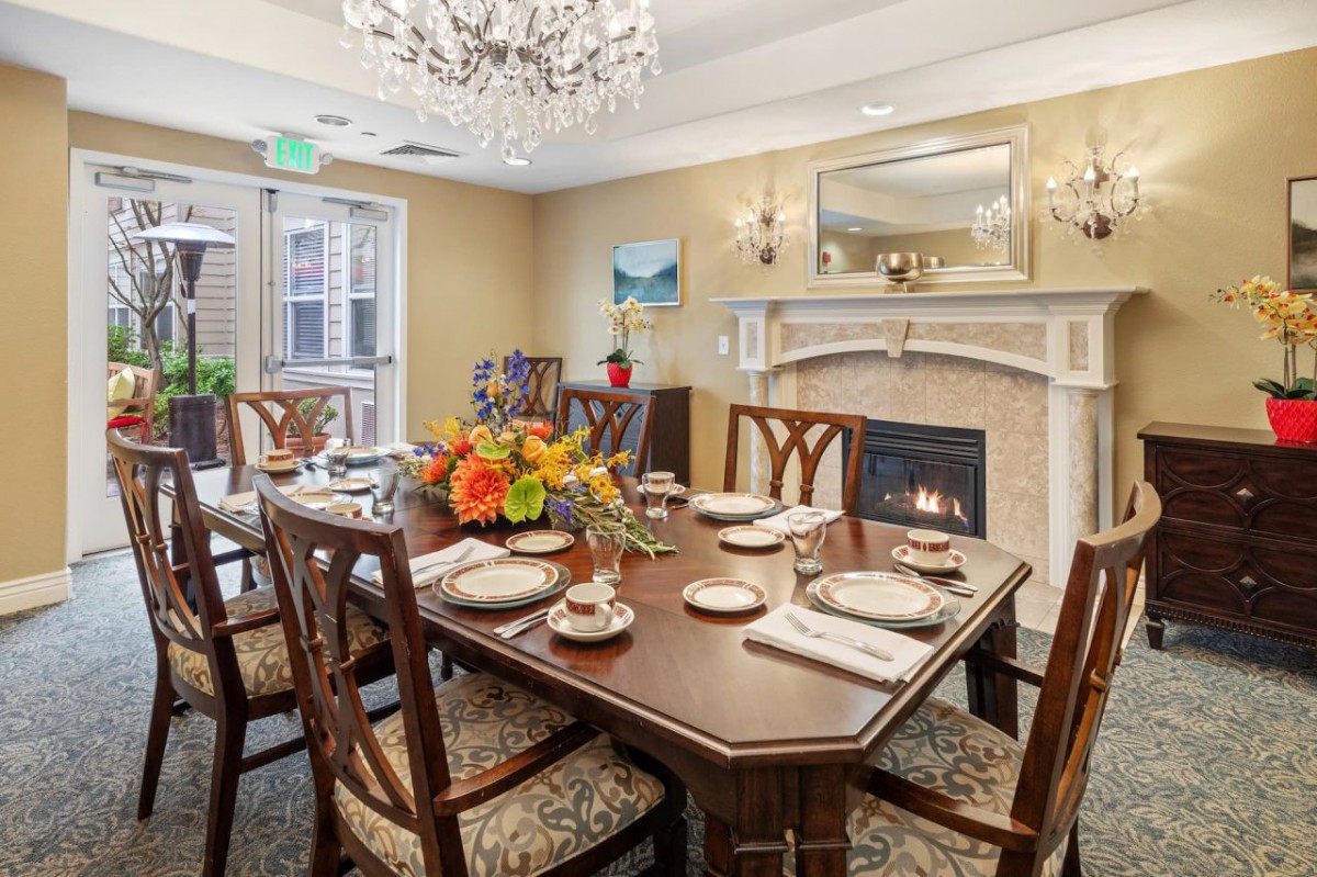 An elegantly decorated dining room featuring a set table, chandelier, and fireplace.