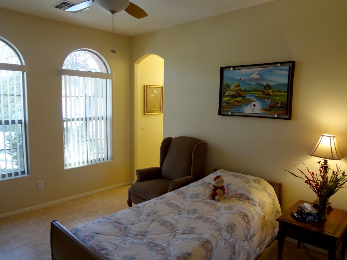 A cozy bedroom with a single bed, an armchair, a window with blinds, and a painting on the wall.