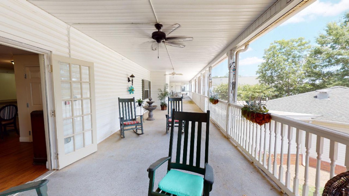 A cozy porch with rocking chairs and potted plants, featuring a ceiling fan and white siding.