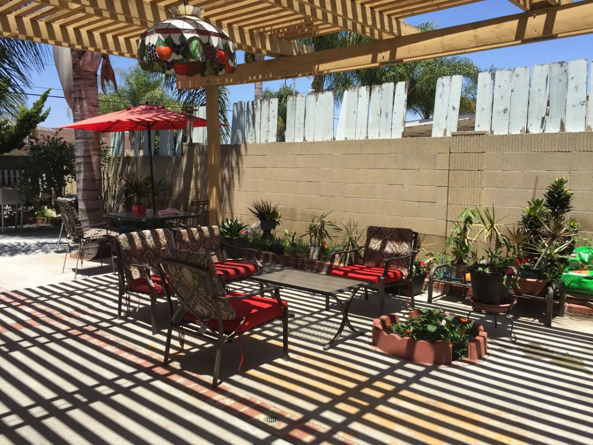 A sunny patio with furniture and plants, featuring a large umbrella casting shadows.