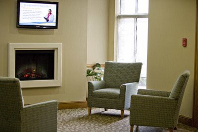 A cozy waiting room with comfortable chairs, a wall-mounted television, and natural lighting from large windows.