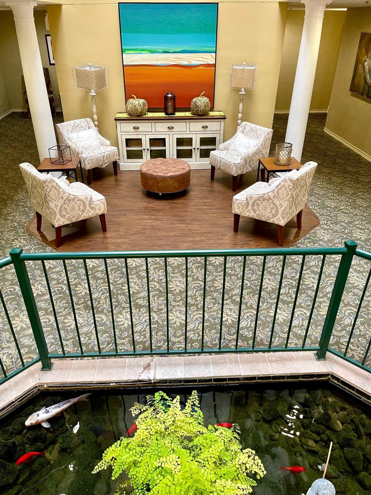 A cozy lobby area with plush chairs and a central coffee table, overlooking an indoor pond.