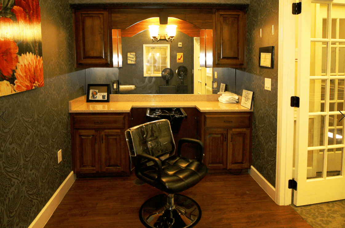 A cozy barbershop setup with a classic barber chair facing a well-lit vanity mirror and surrounded by wooden cabinets.