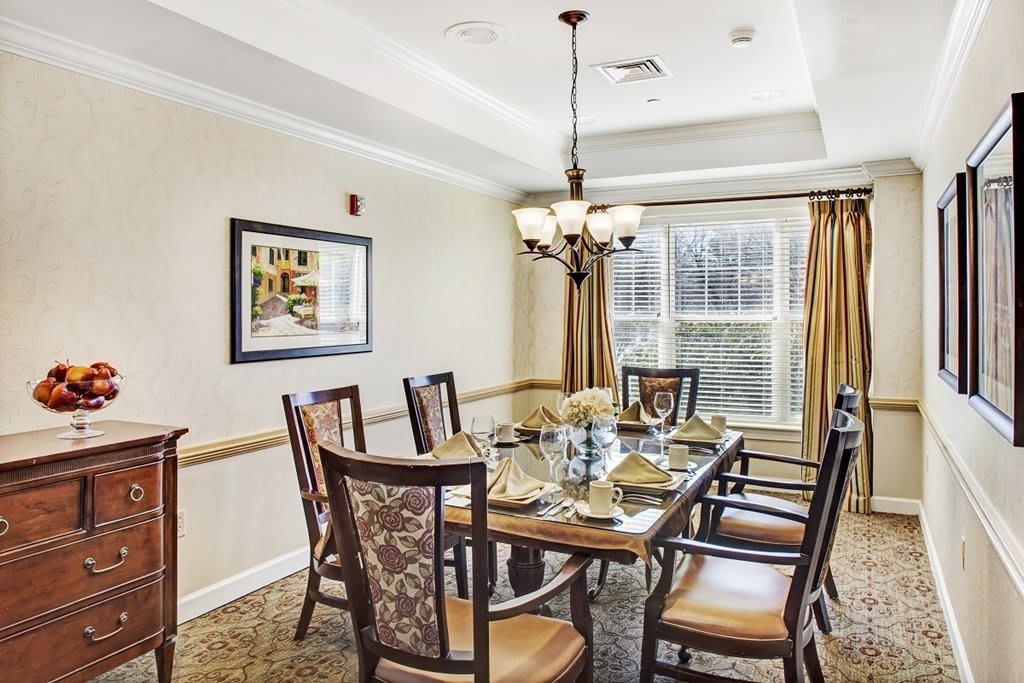 A well-decorated dining room featuring a long table, elegant chairs, and a chandelier under a tray ceiling.
