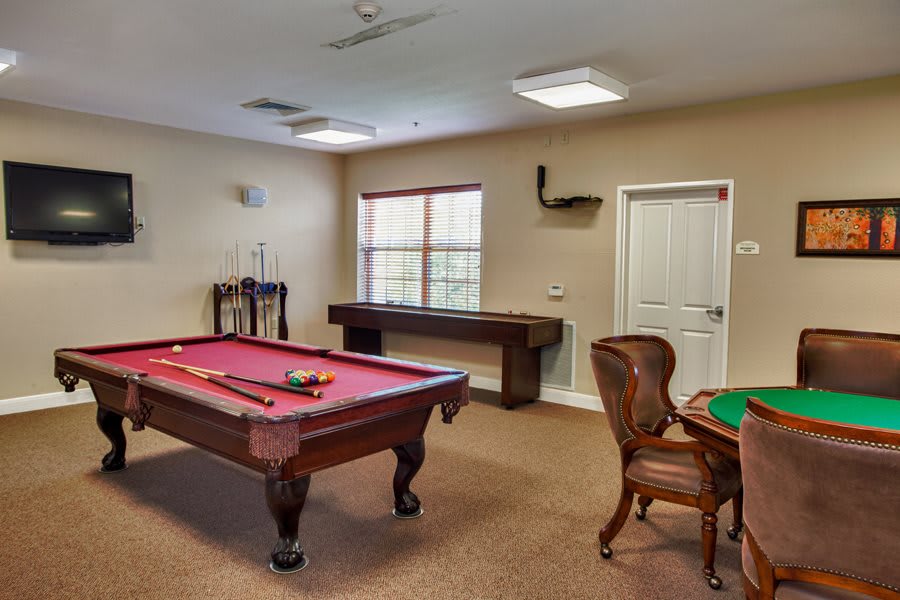 A cozy game room featuring a pool table, shuffleboard, and a card table with chairs.