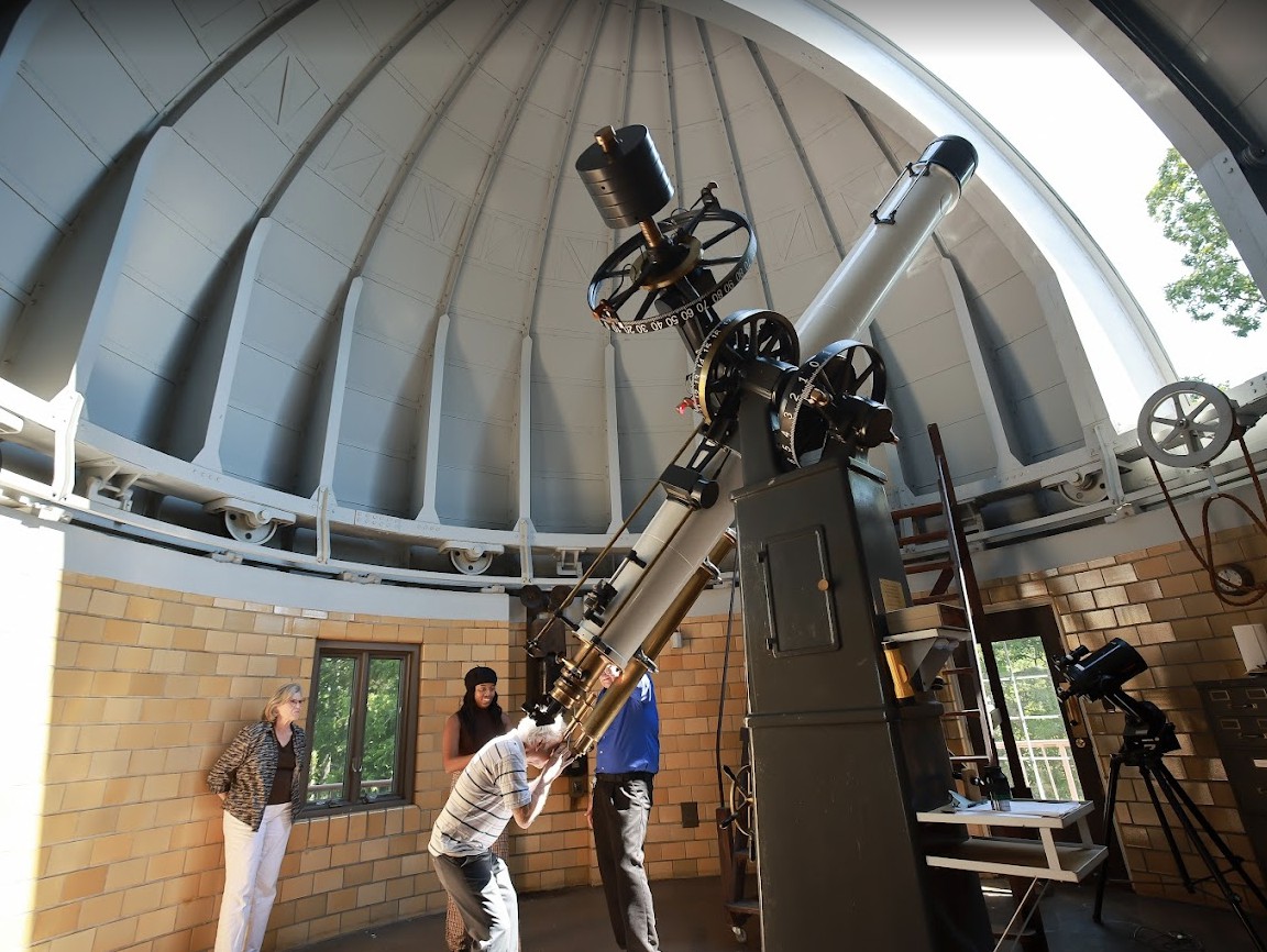 People observing through a telescope inside an observatory dome.