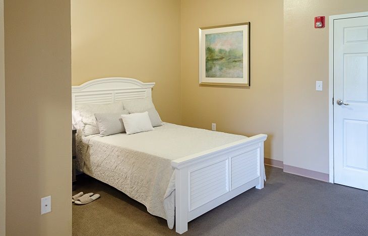 A minimalist bedroom with a white bed and a framed picture on the wall.