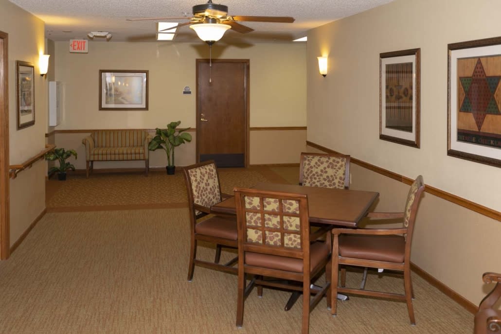 A cozy waiting area with a table and chairs, carpeted flooring, and wall art.