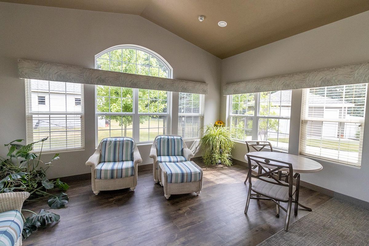 A bright and airy living room featuring two striped chairs, large windows, and a small dining area.