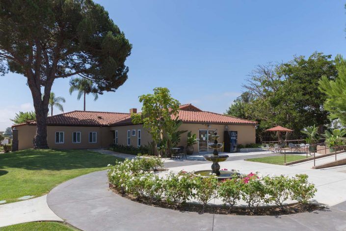 A charming house with a red-tiled roof surrounded by a lush garden and a central fountain.