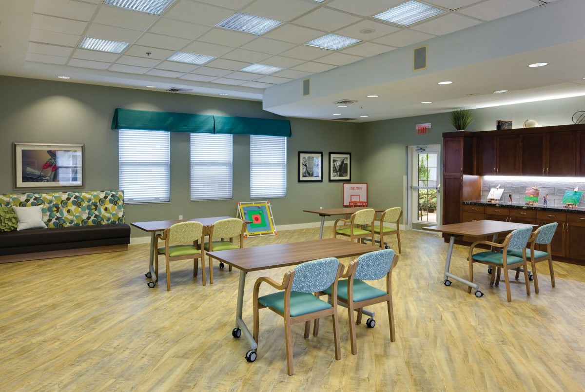 A spacious dining room with tables and chairs, featuring large windows and bright lighting.