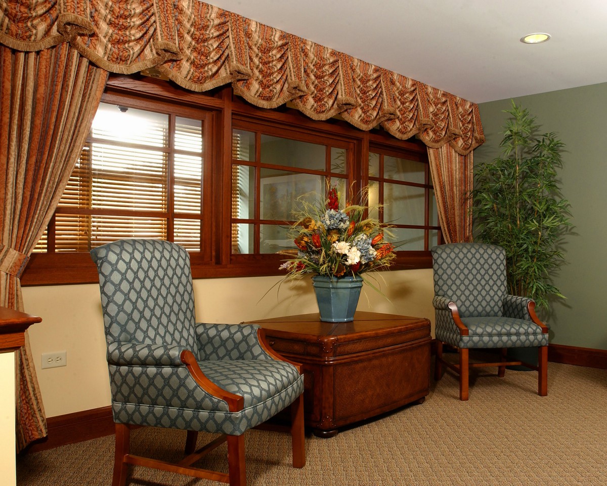 A cozy living room with two patterned chairs, a wooden table, and floral decorations by the window.