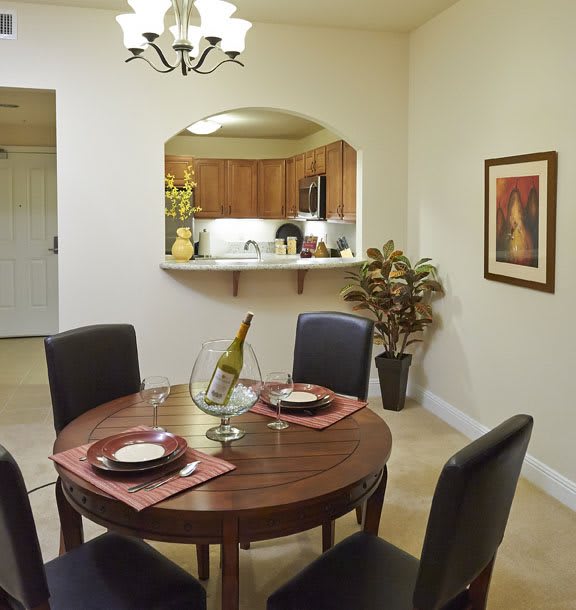A cozy dining room with a round table set for two, featuring a view into the kitchen.