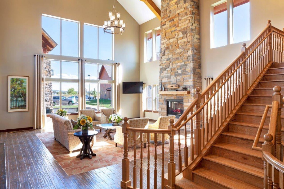 A spacious living room featuring a stone fireplace, large windows, and a wooden staircase.