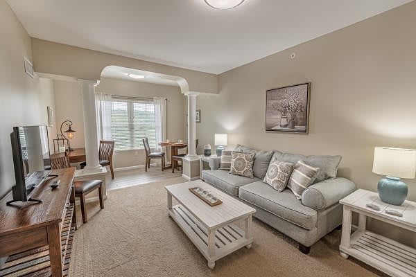 A cozy living room with a sofa, coffee table, and adjoining dining area, featuring neutral tones and soft lighting.