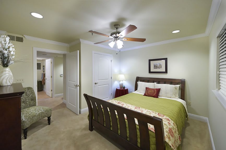 A cozy bedroom featuring a wooden bed with green bedding, a ceiling fan, and soft lighting.