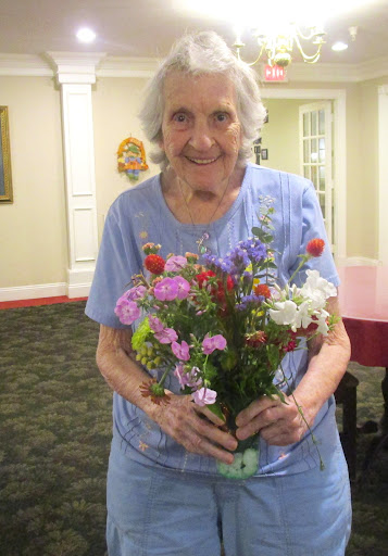 An elderly woman happily holding a bouquet of colorful flowers.