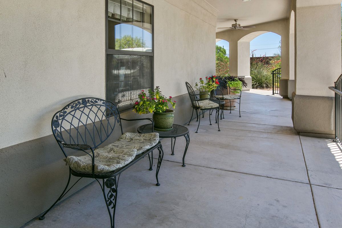 A covered porch with metal chairs, tables, and potted plants.