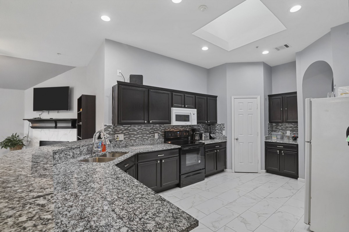 A modern kitchen featuring dark cabinets, granite countertops, and recessed lighting.